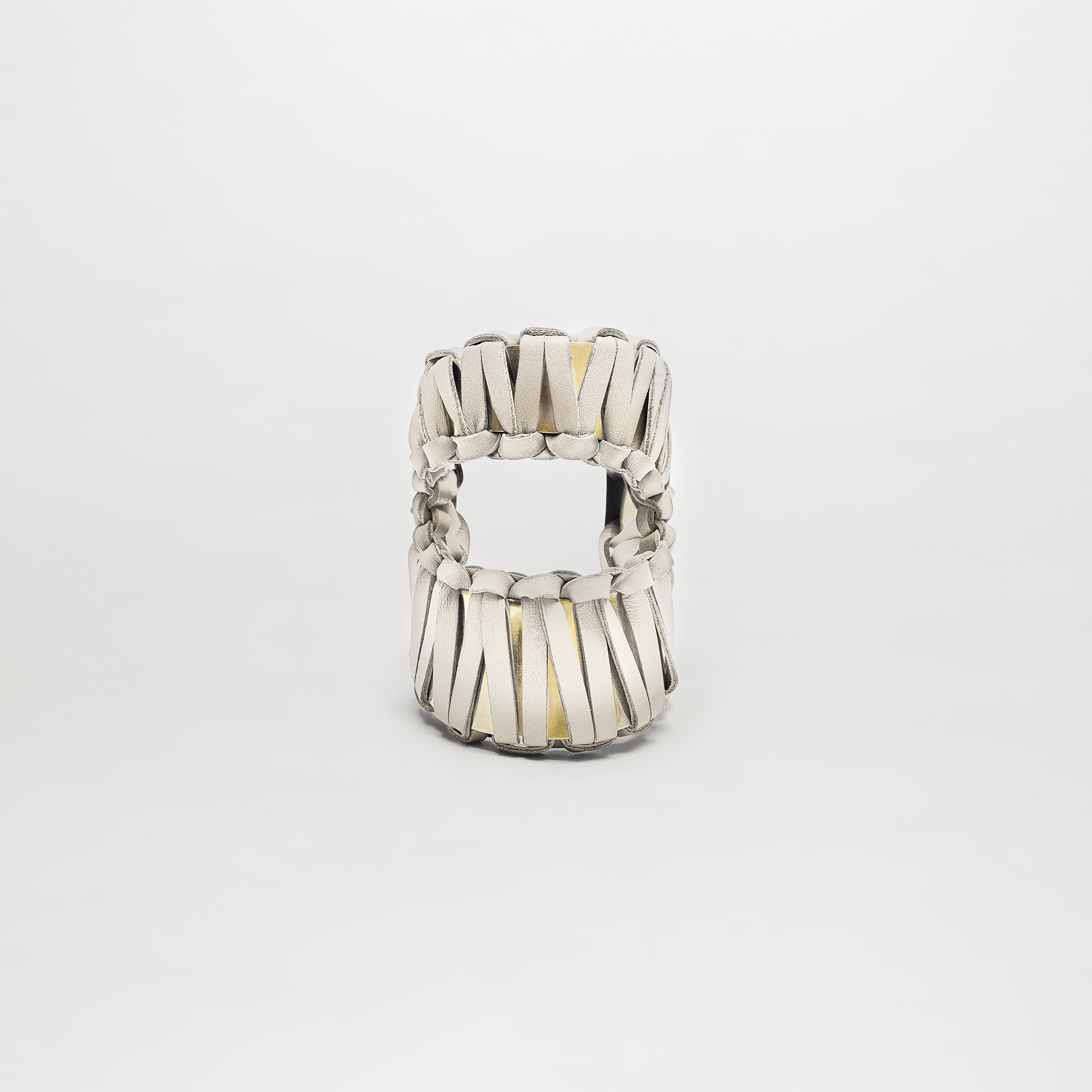 The Majel Cuff is a white sandal featuring thick, woven leather straps and a subtle gold-plated buckle, shown from the front against a plain white background.