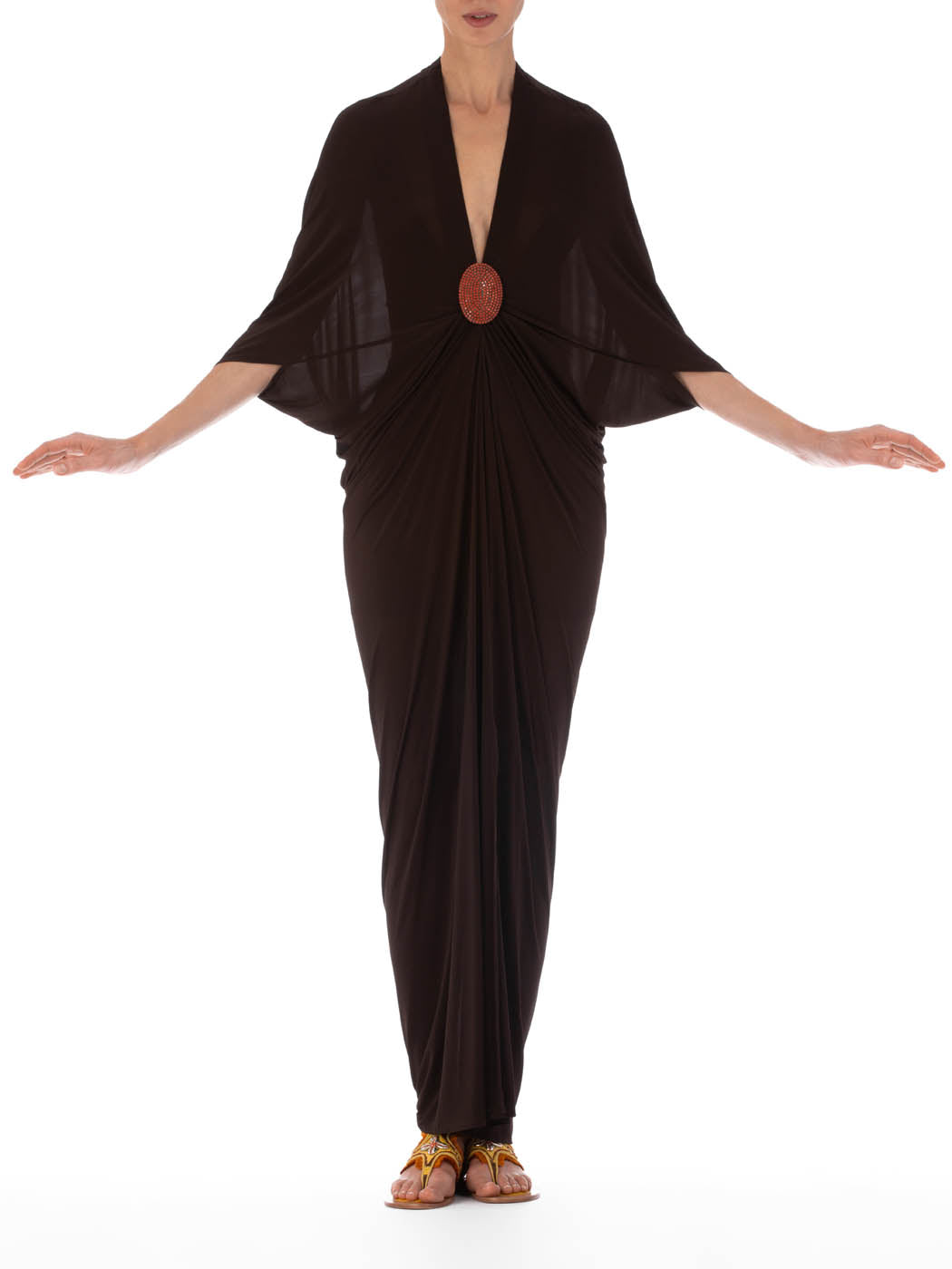 The Malu Dress Brown with draped sleeves and a decorative orange brooch at the waist, featuring a deep V neckline, displayed against a white background.