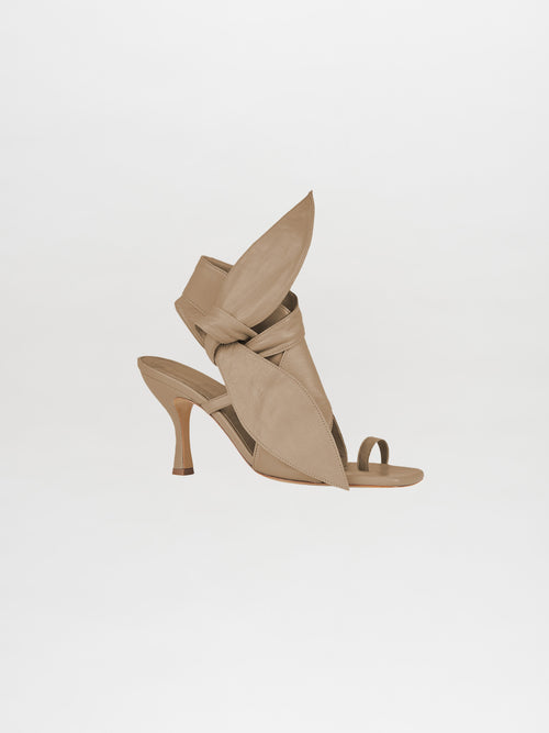 The Marco Heel Camel is a trendy high-heeled sandal crafted from Italian calf leather, featuring a crisscross design and an open toe, set against a beige background.