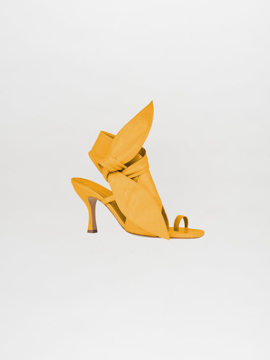 The Marco Heel Yellow from the Silvia Tcherassi collection features a stunning high-heeled sandal crafted from exquisite Italian calf leather with a unique folded design, showcased against a white background.