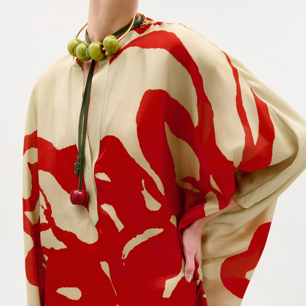 Person wearing a red and beige patterned garment with a necklace.