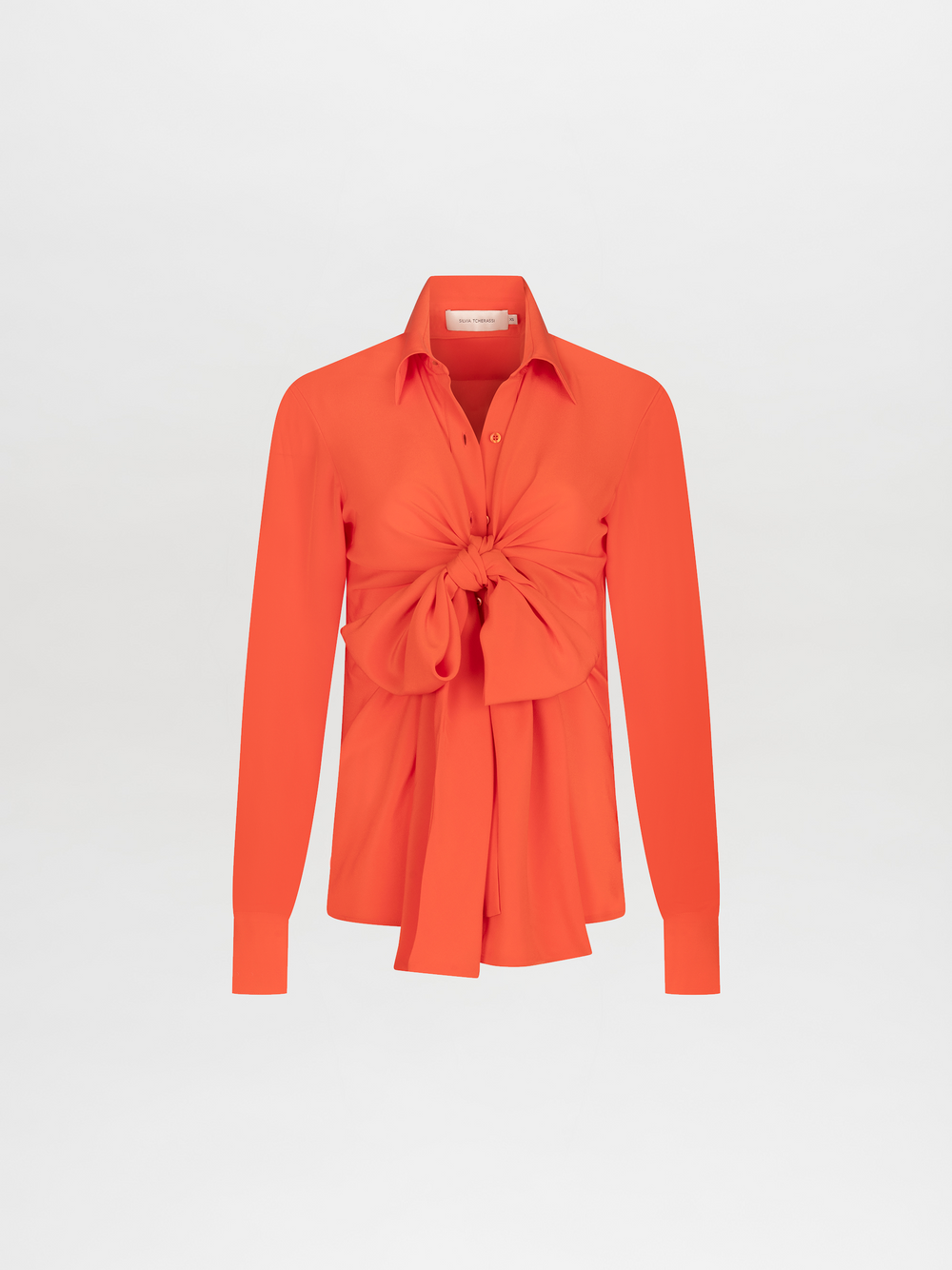 The Mercury Blouse Tangerine is a vibrant orange silk top with long sleeves, a collar, button-down front, and an oversized front knot at the waist, shown on a plain white background.