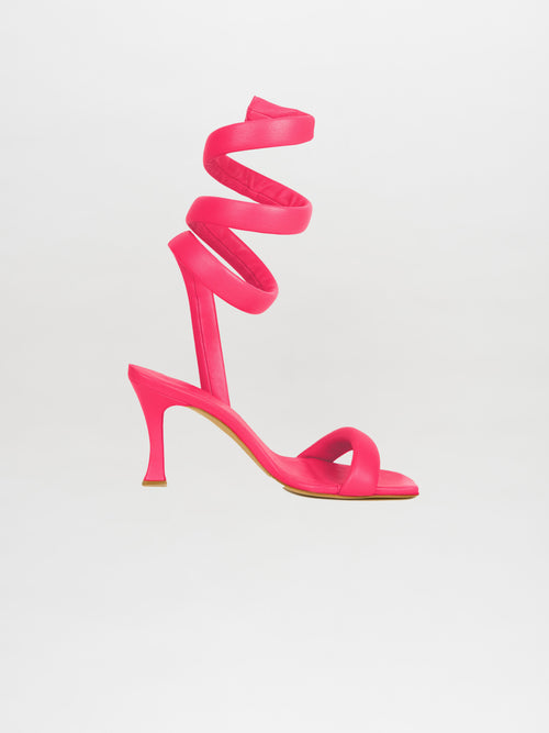 The Mika Heels Orchid is a vibrant pink high-heeled sandal made from Italian calf leather, showcasing a spiral ankle wrap design against a white background.