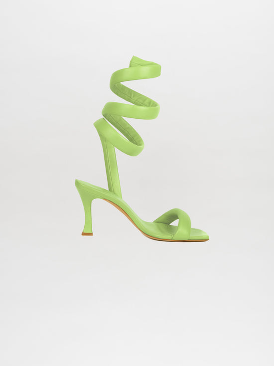 The Mika Heels Green, crafted from luxurious Italian calf leather in a striking lime color, showcase a spiral ankle strap against a light background—a perfect choice for trendsetters.