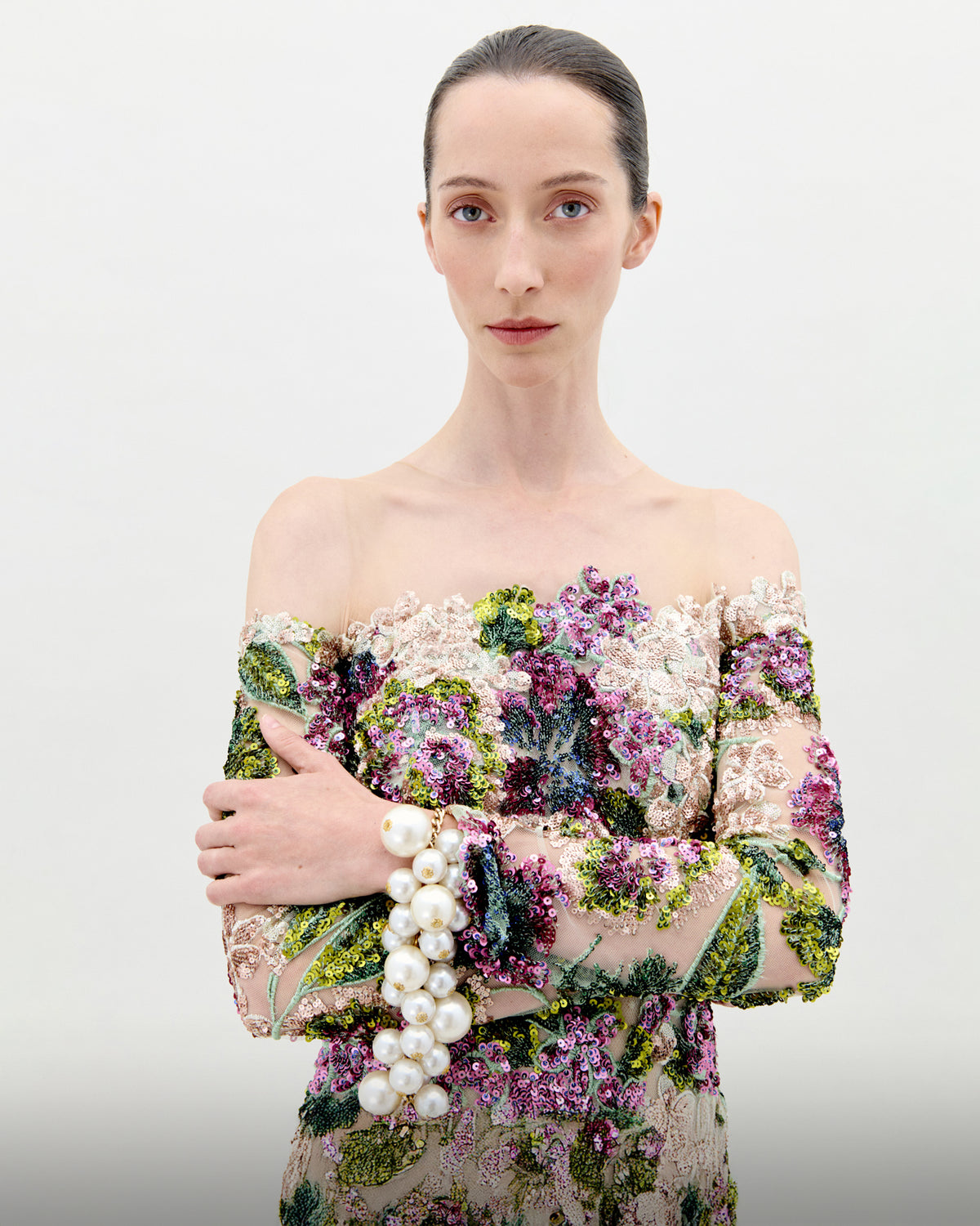 Woman wearing a floral off-shoulder dress with pearls on a plain background