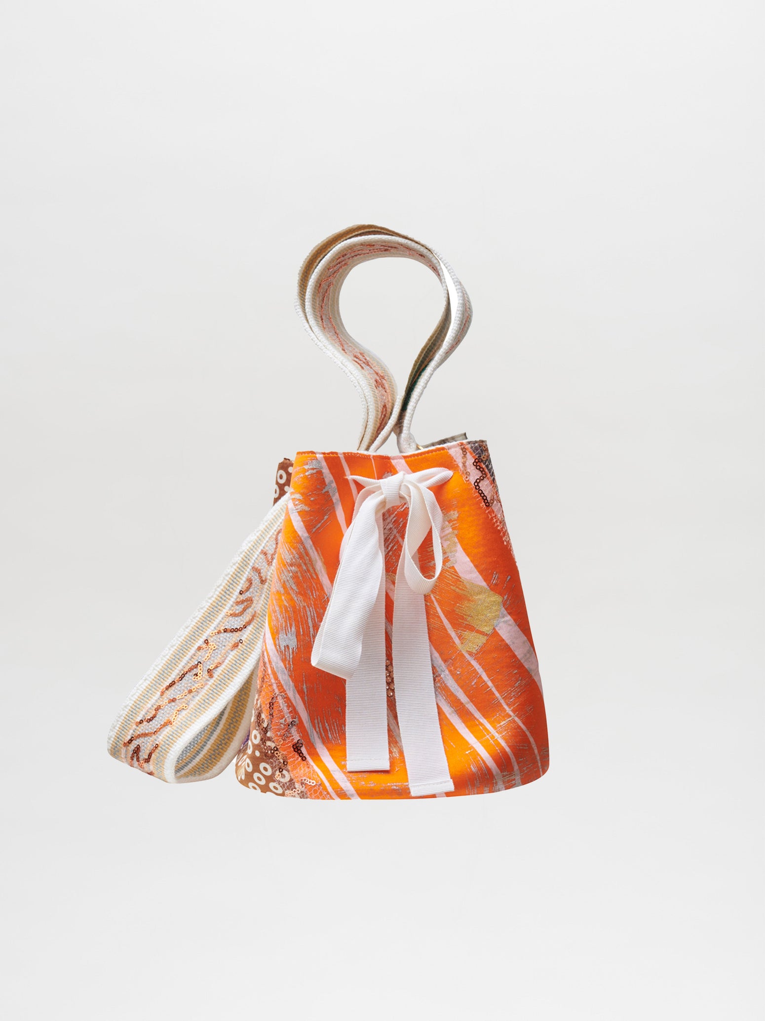 An orange and white patterned drawstring Mochila Laaput Beige handbag with a hand-woven strap and a white bow, isolated on a white background.