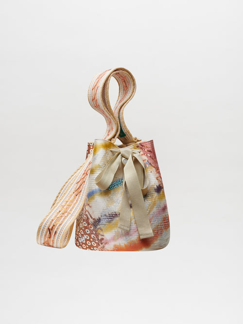 Colorful patterned Mochila Laaput Pearl handbag with a bow and braided strap against a white background.