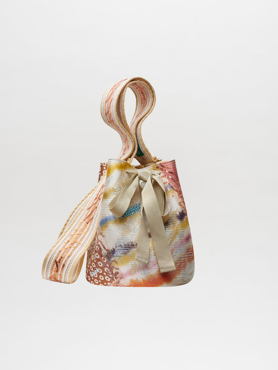 Colorful patterned Mochila Laaput Pearl handbag with a bow and braided strap against a white background.