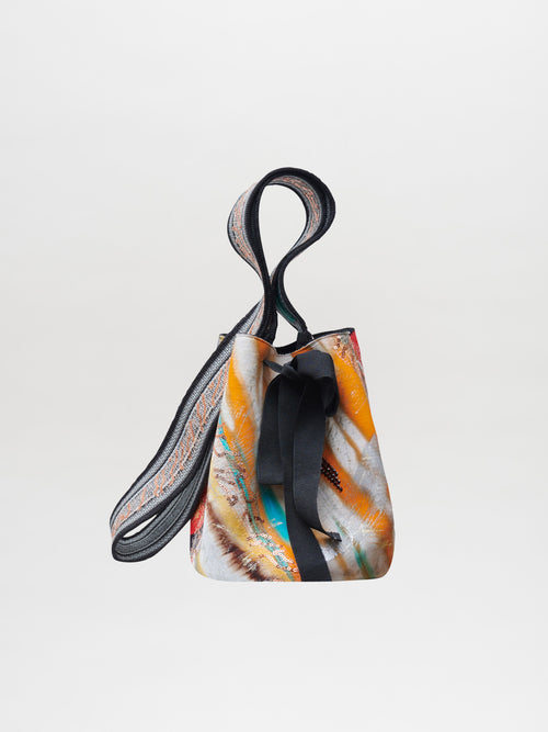 The Mochila Laaput Black, a vibrant drawstring handbag featuring an abstract pattern and secured with a black ribbon closure, is displayed against a plain background, highlighting the exquisite craftsmanship of the Wayuu artisans.