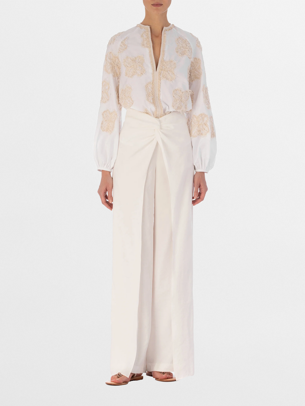 Rear view of a person with long hair wearing the Molveno Blouse Cream Flowers, featuring embroidered floral motifs, paired with high-waisted, wide-leg pants.