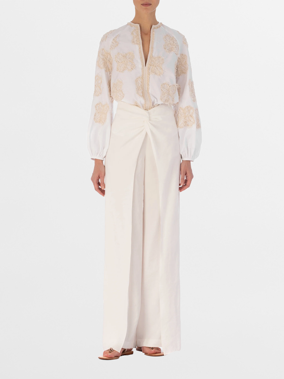 Rear view of a person with long hair wearing the Molveno Blouse Cream Flowers, featuring embroidered floral motifs, paired with high-waisted, wide-leg pants.