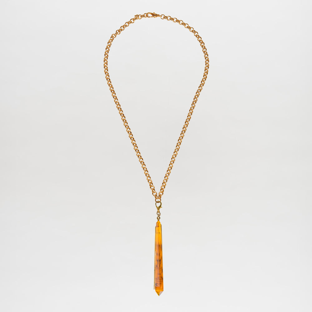 The Montse Necklace is a gold chain layering piece featuring a geometric amber crystal pendant, elegantly centered and crafted in Italy, shown against a plain white background.