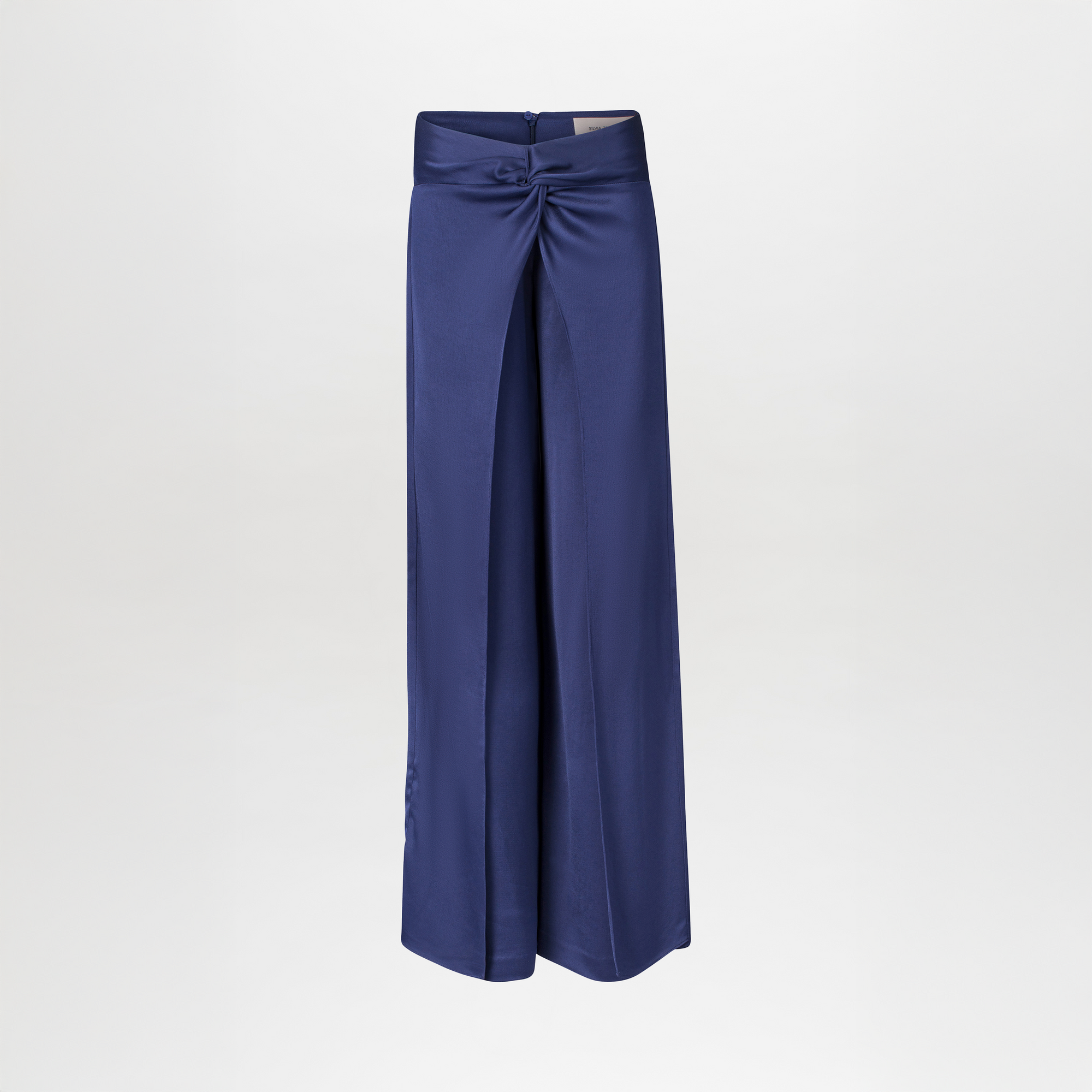 The Nadira Pant is a high-waisted, wide-leg navy hammered silk pant with a front slit and decorative knot detail at the waistband, displayed on a plain white background.