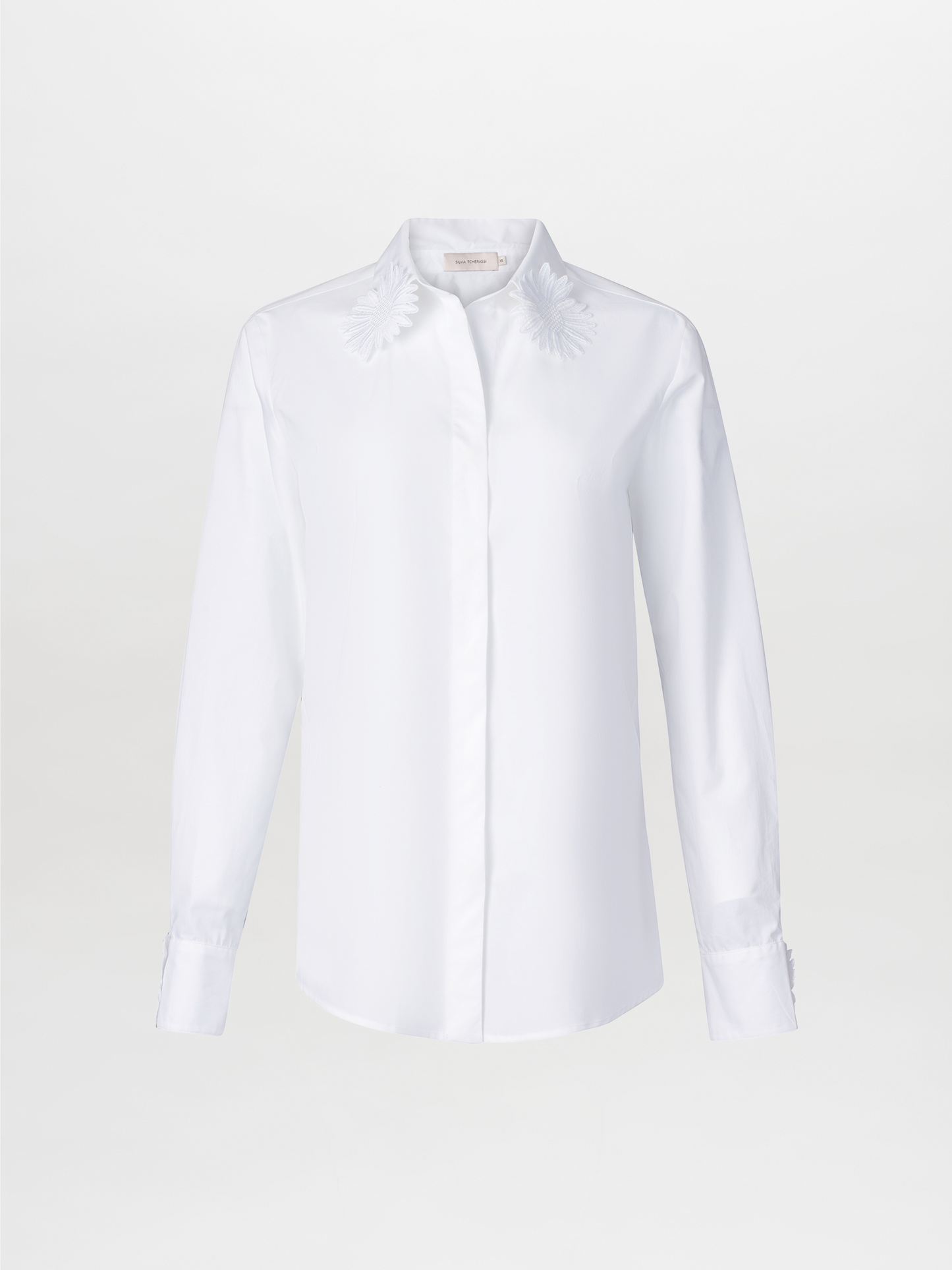 Naroa Blouse White features a long-sleeve cotton design with floral embroidery on the classic shirt collar, set against a plain white backdrop.