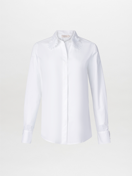 Naroa Blouse White features a long-sleeve cotton design with floral embroidery on the classic shirt collar, set against a plain white backdrop.