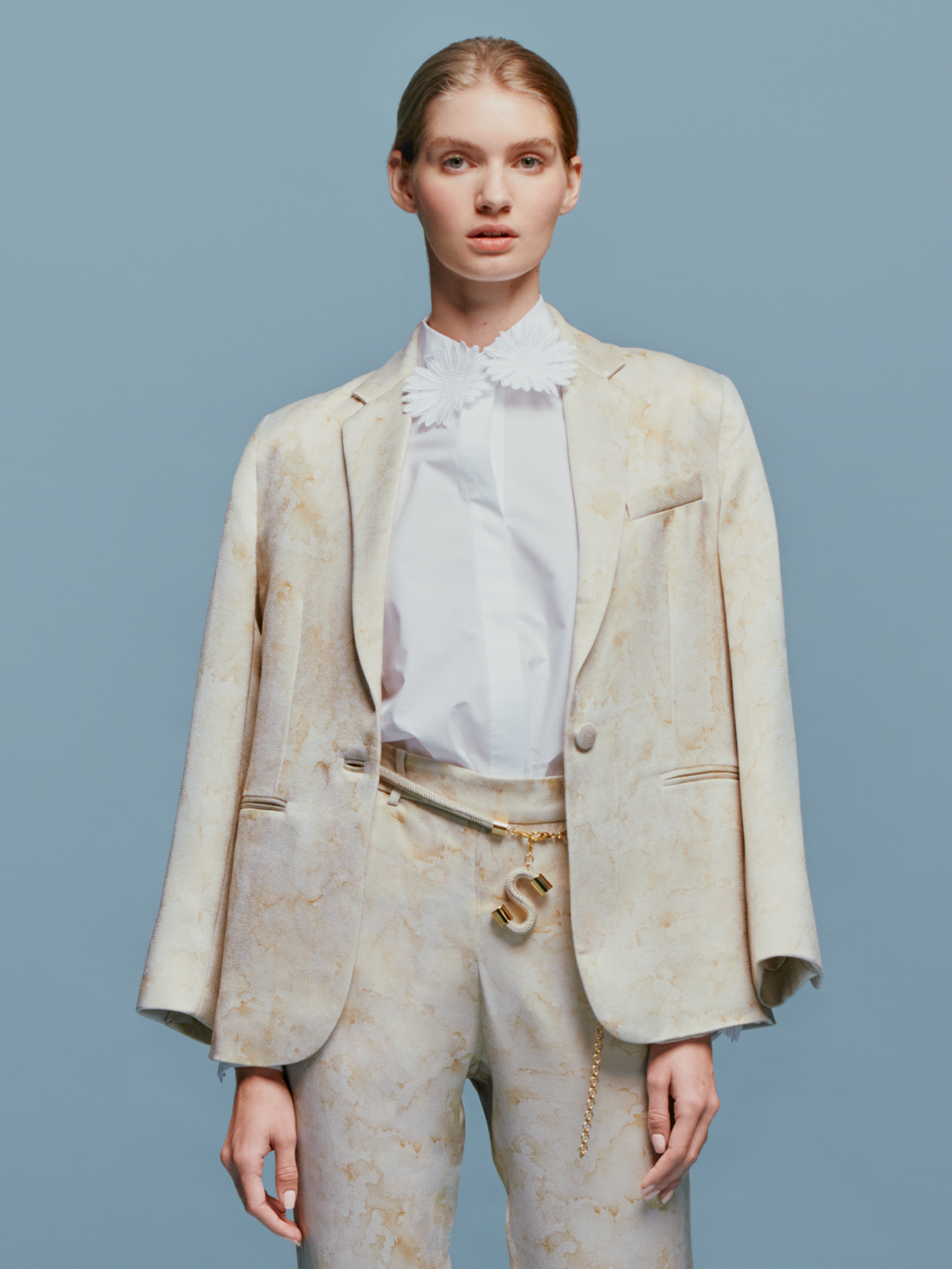 Person dressed in the Naroa Blouse White with a floral shirt and gold belt, standing against a blue background, ready to celebrate September 2nd.