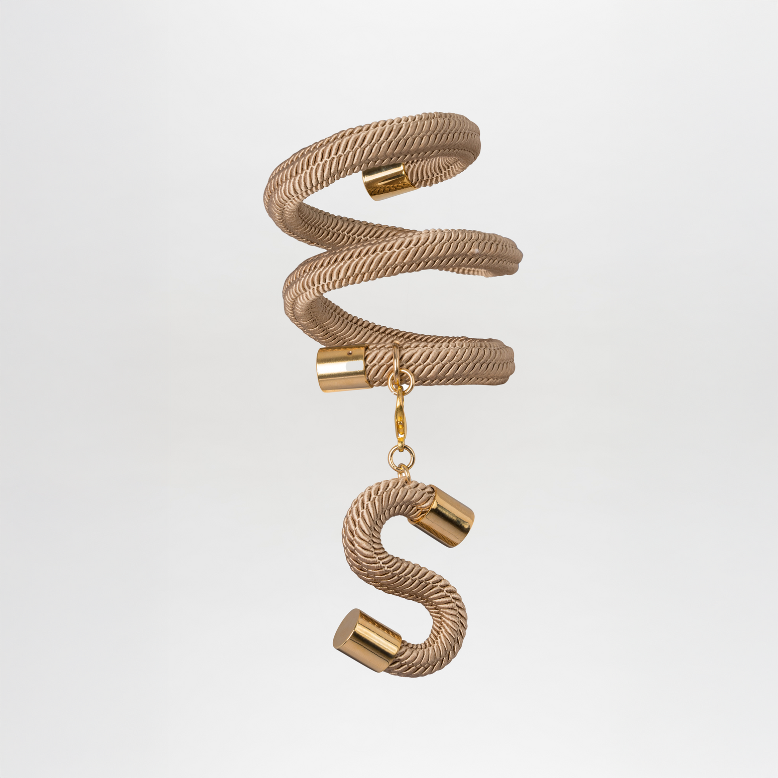 The Nicky Bracelet, crafted from gold-plated brass, exhibits a spiral-shaped pendant with a textured metallic finish and gold accents. It features an elegant hanging "S" charm, embodying elegance and sophistication in Tcherassi's design.