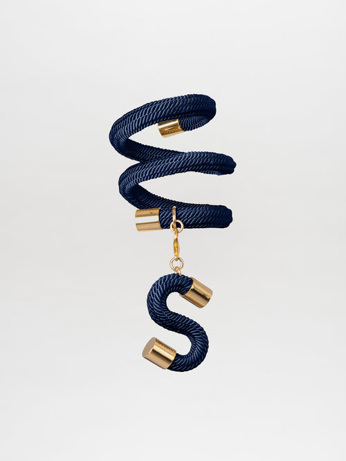 The Nicky Bracelet Navy by Tcherassi features an elegant spiral design that gracefully descends into an S-shaped curve, with both ends and the base adorned in luxurious gold-plated brass.