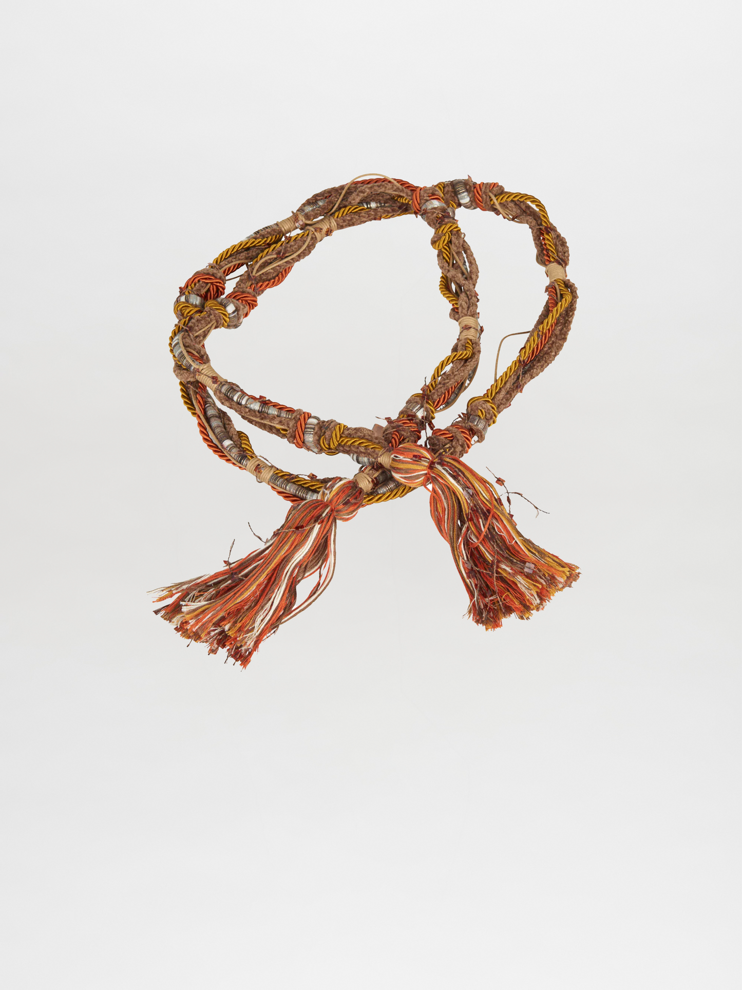 The Nellie Belt Amber, a multicolored woven cord with tassels featuring intertwined threads in shades of orange, yellow, and amber hues from Pre Fall 2023, is displayed on a plain white background.