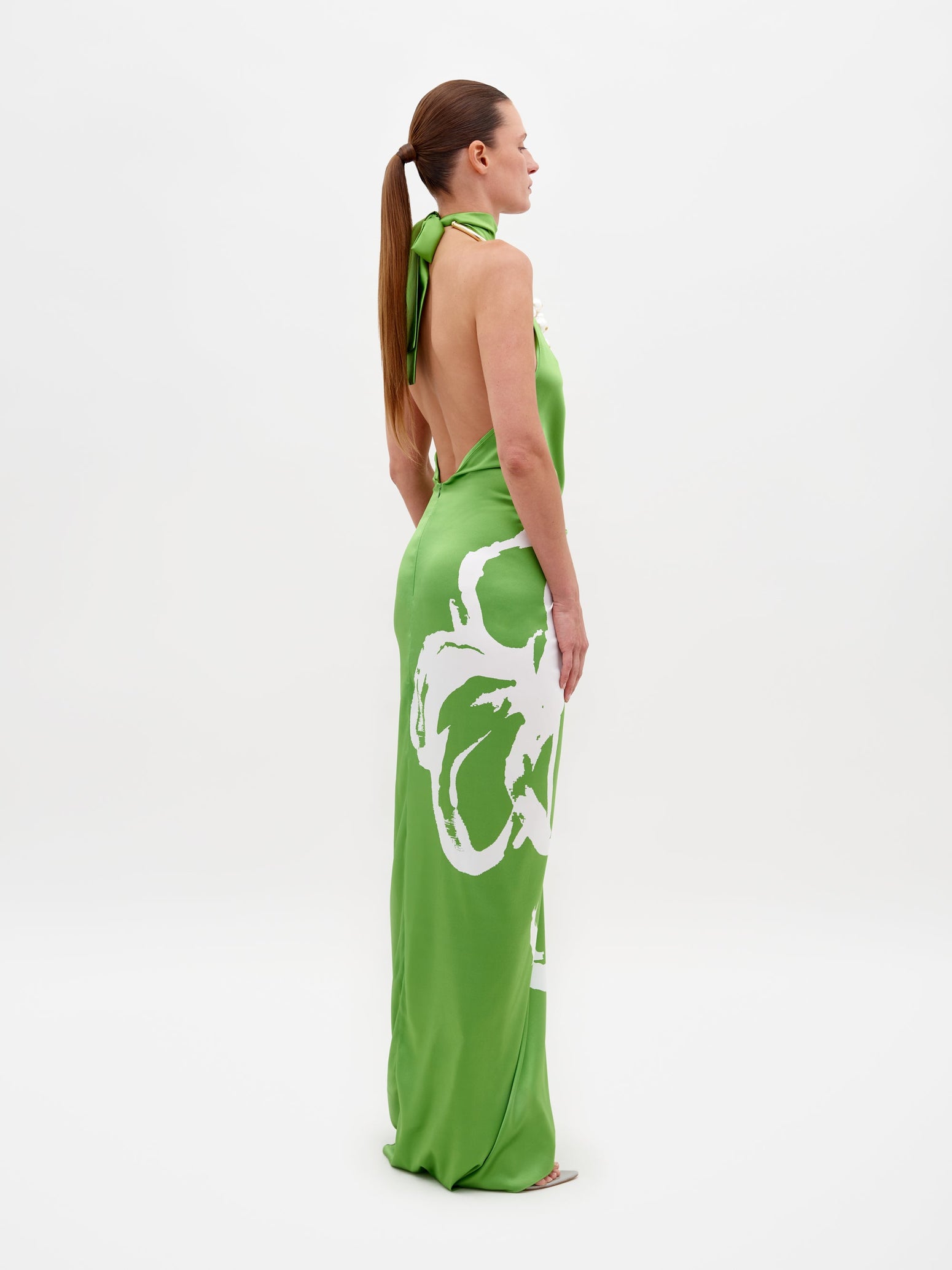 A person stands against a white background, wearing the Olatz Dress, a sleeveless green ensemble with an abstract print and front knot. The dress flows effortlessly, blending elegance with modern style.