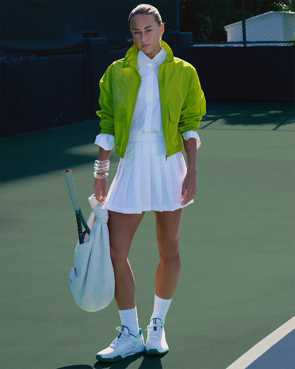 Tennis player in a green jacket and white outfit on a tennis court