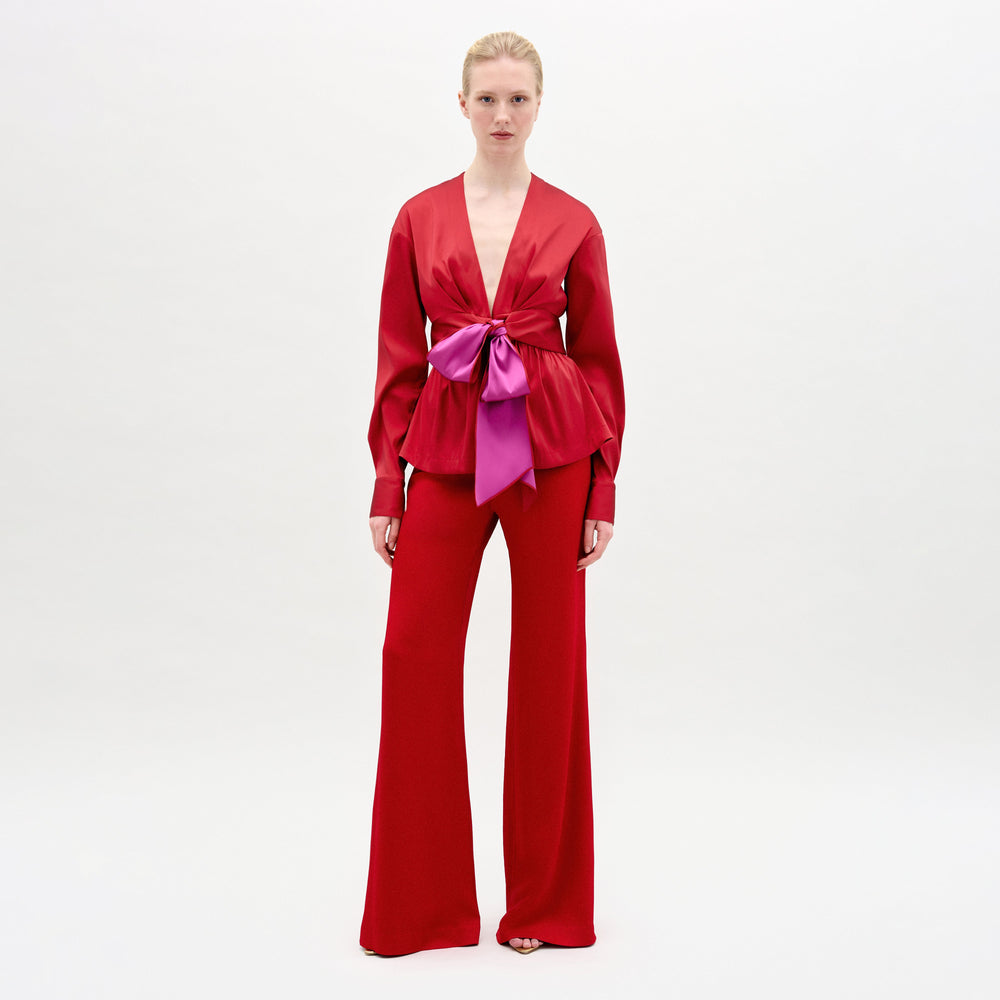 A woman wearing the Palermo pant in color rouge and the Sanvi blouse on a white background