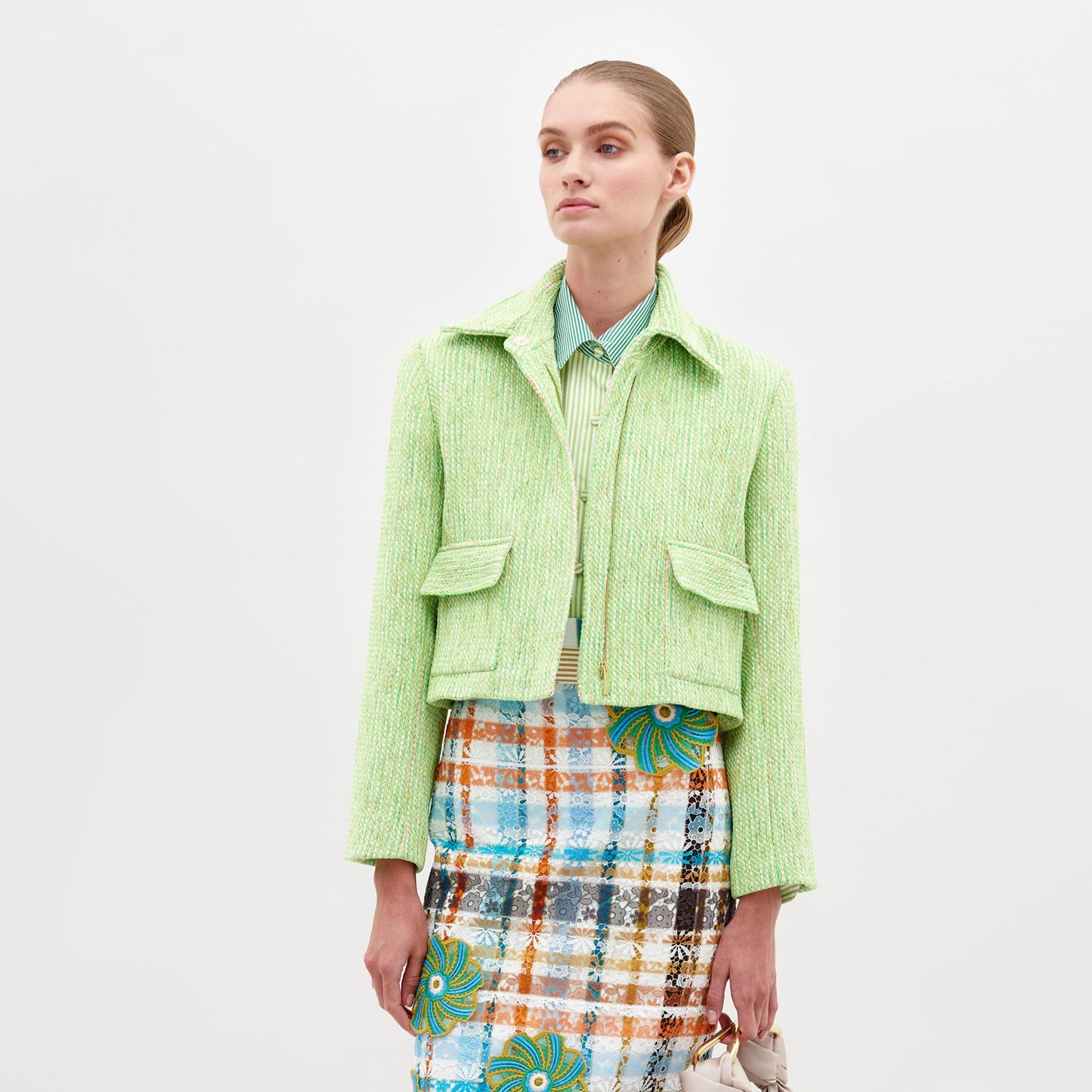 Person wearing the Perla Jacket Lime over a striped shirt and a colorful patterned skirt against a plain white background, showcasing a pre-order fashion piece for 2025.