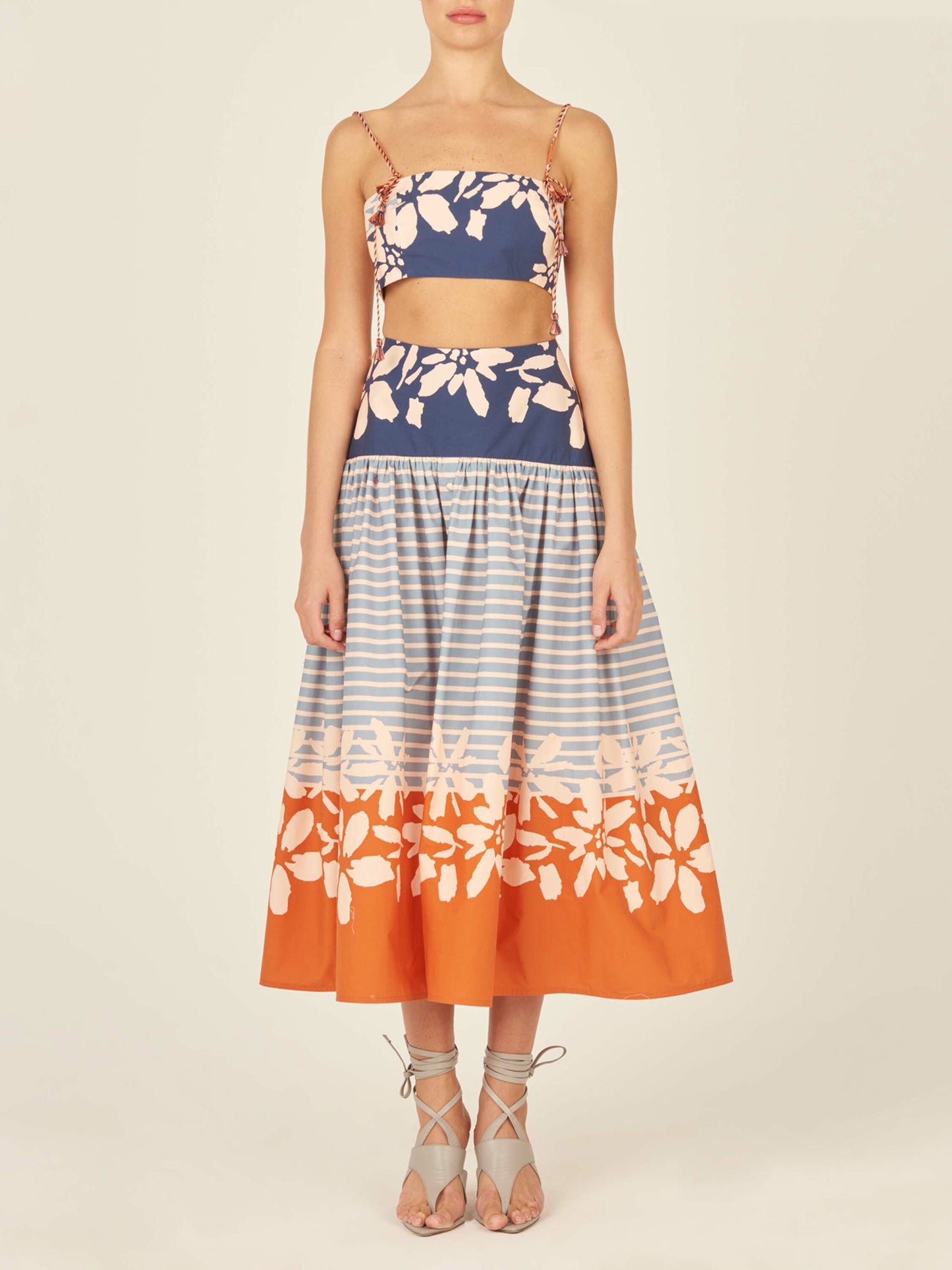 The Apia Skirt Celeste Orange is a flared midi design that features horizontal blue stripes and a wide blue and white floral band at the top. The hem is embellished with an eye-catching celeste orange floral border.