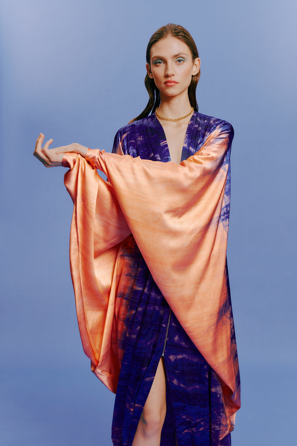 A person wearing a colorful, flowing robe poses against a blue background.