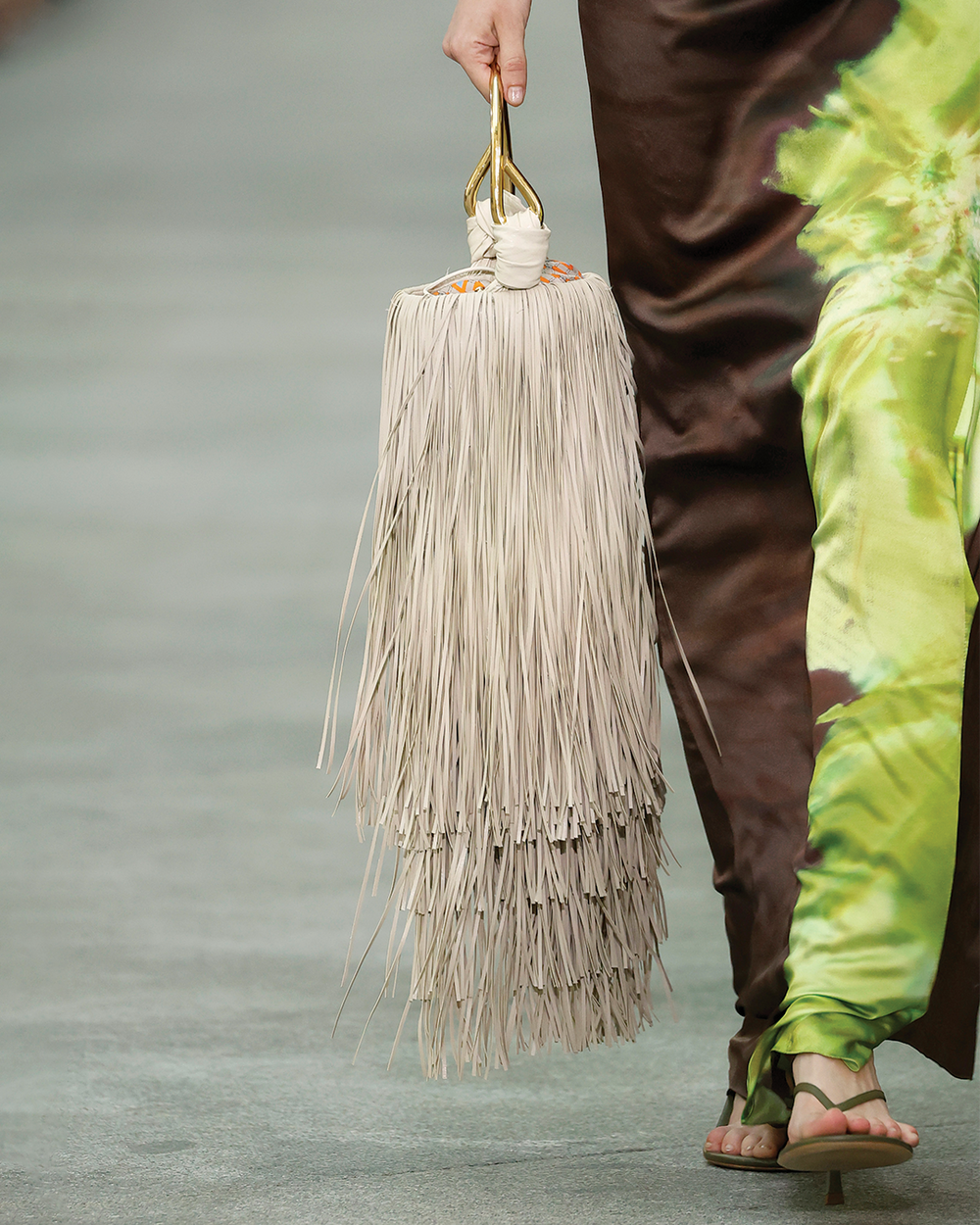Person holding a beige fringe bag with a neutral background