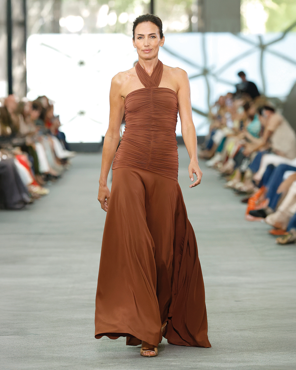 Model wearing a brown halter neck dress on a fashion runway.
