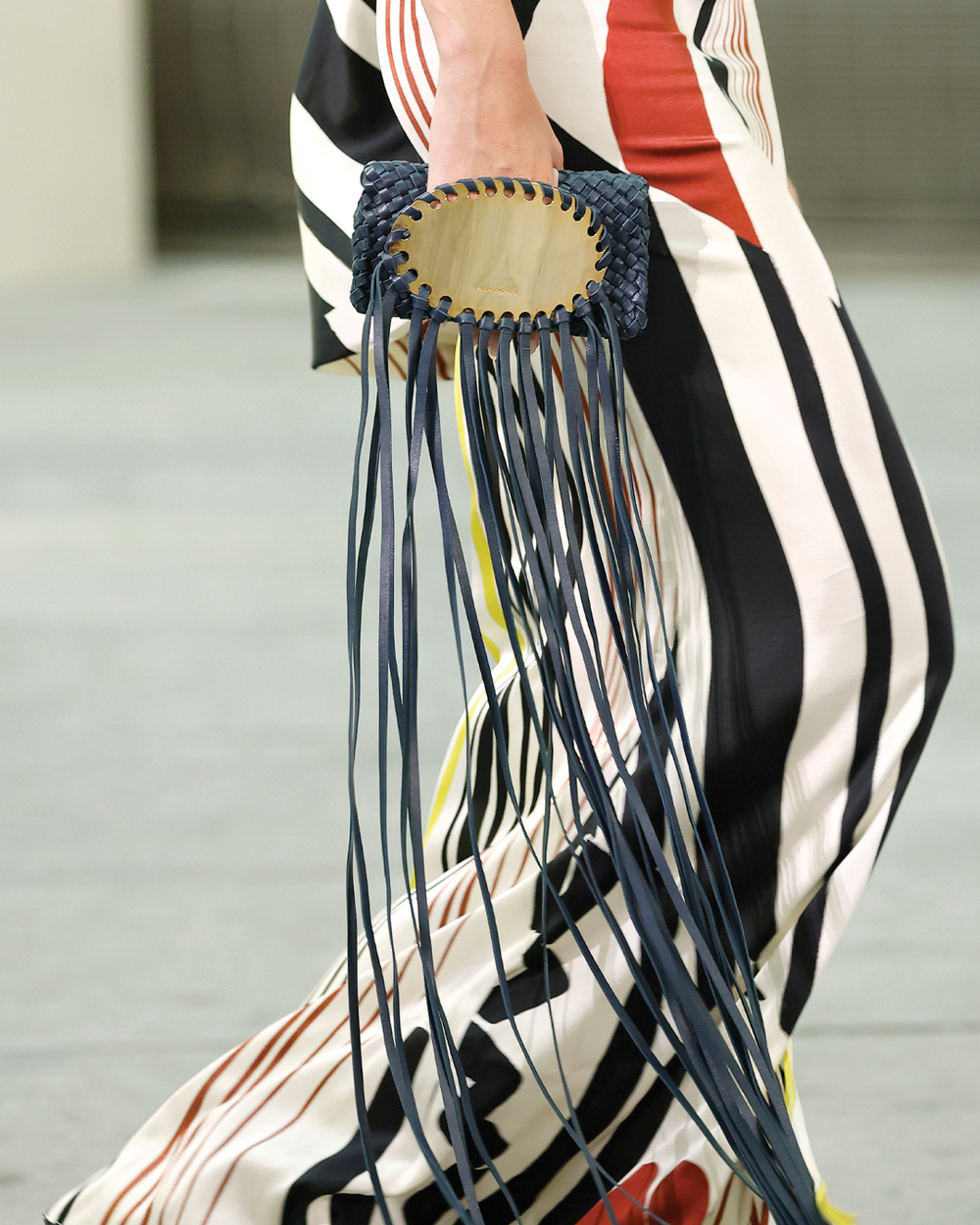 Close-up of a hand holding a fringed handbag with a blurred background