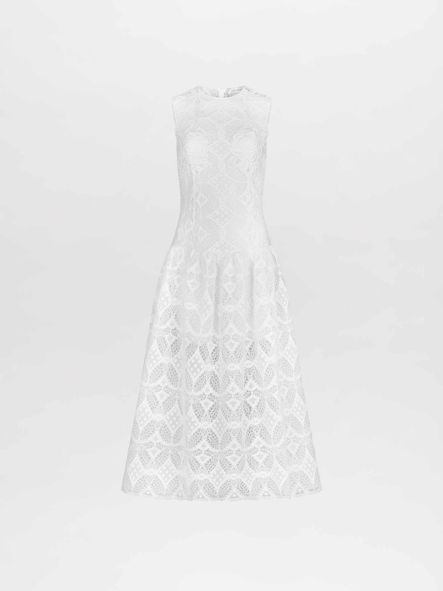 A person stands in the Paola Dress White, featuring a sleeveless lace design with a flared skirt, complemented by brown lace-up sandals. This item is available for pre-order and will ship by February 15th, 2025. The background is plain white.