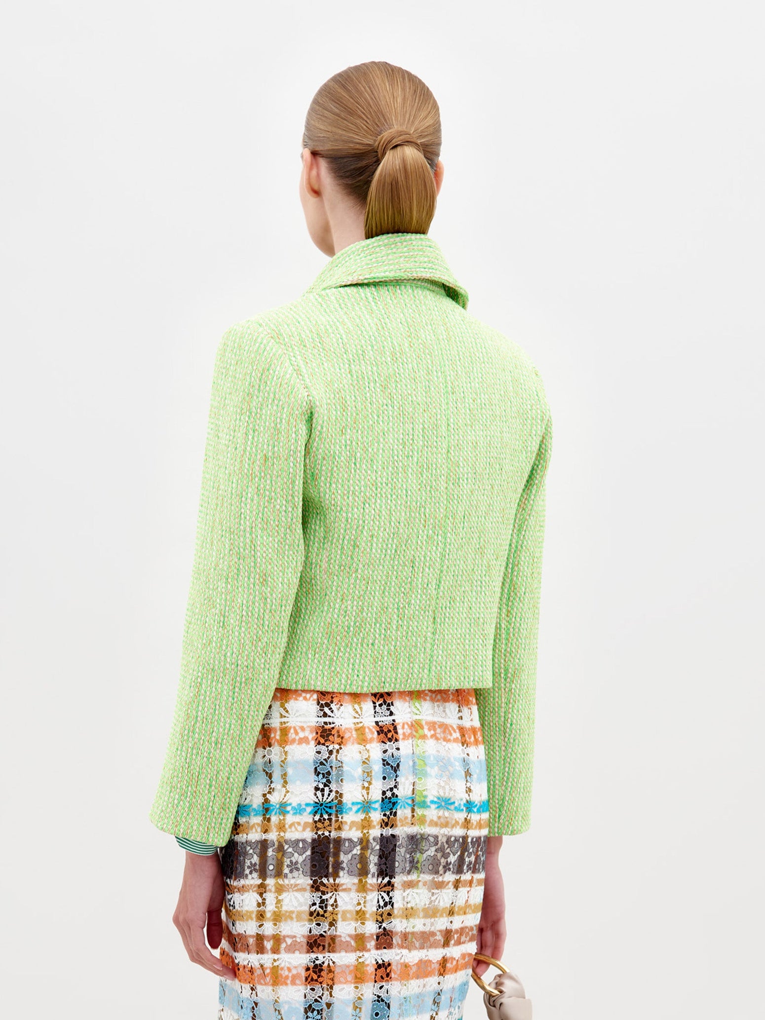 Person wearing the Perla Jacket Lime over a striped shirt and a colorful patterned skirt against a plain white background, showcasing a pre-order fashion piece for 2025.