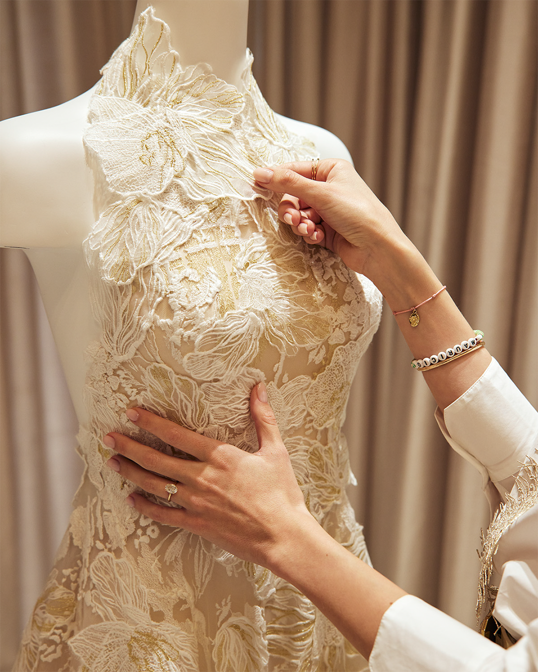 Person adjusting a lace wedding dress on a mannequin.