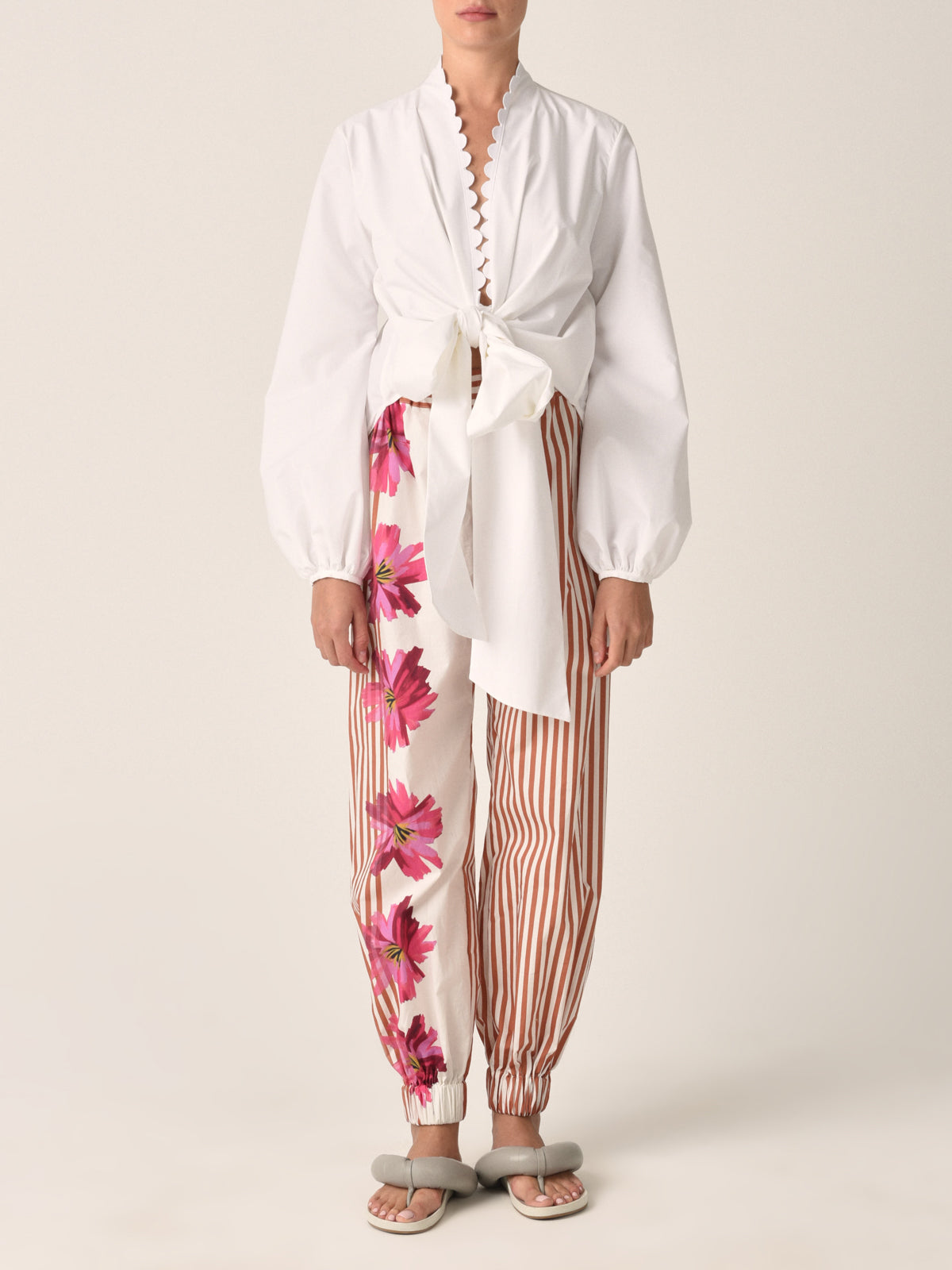 The Chilean Pant Magenta Floral Brushstroke Stripes features light-colored fabric with brown vertical stripes and a magenta floral design on one side. It also comes with an elastic waistband and cuffs for casual luxury.