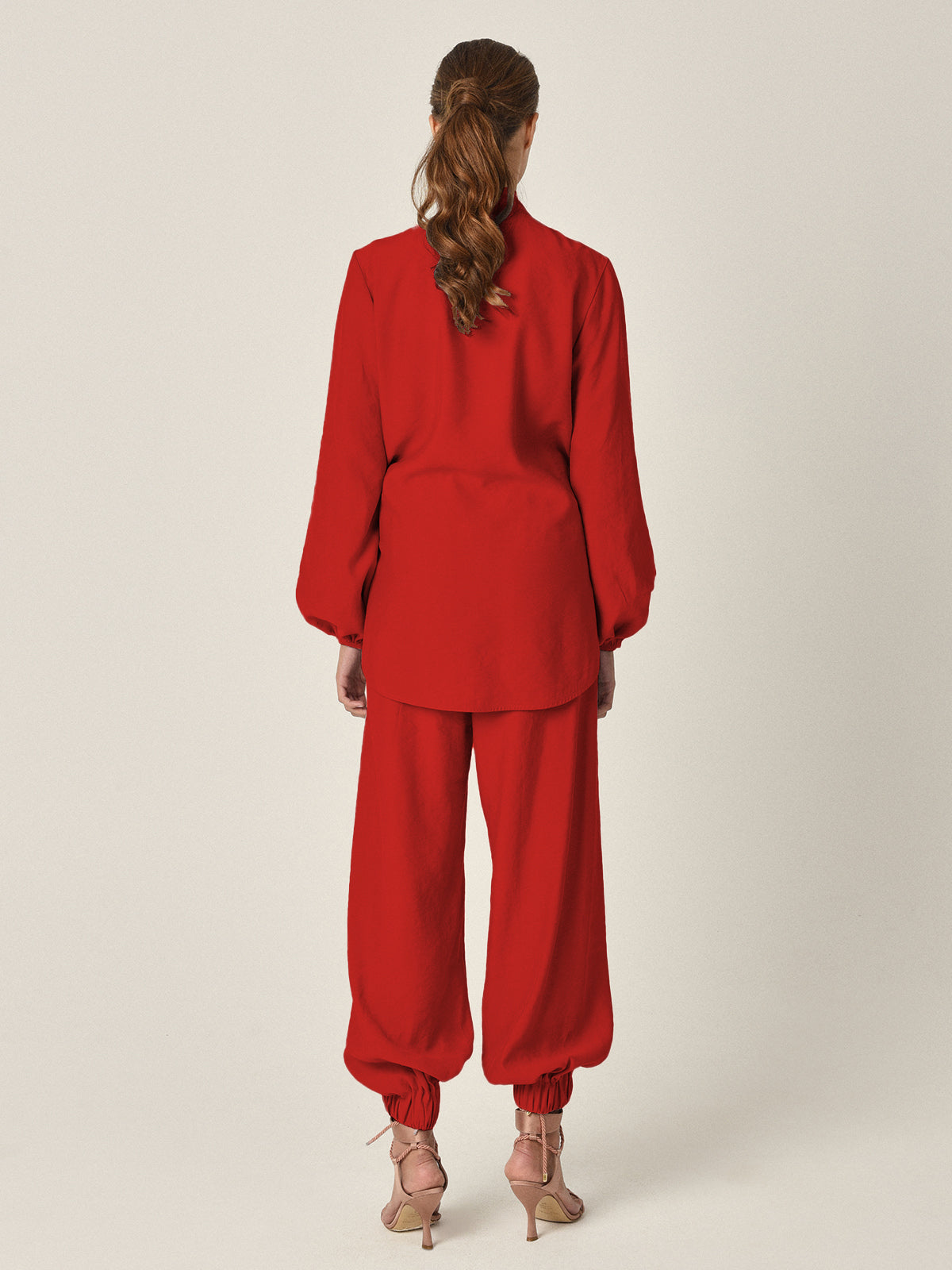 The Honey Blouse Rouge is a vibrant rouge fabric blouse featuring a red long-sleeved design with a large front knot, bishop sleeves with elastic cuffs, and a plunging neckline.