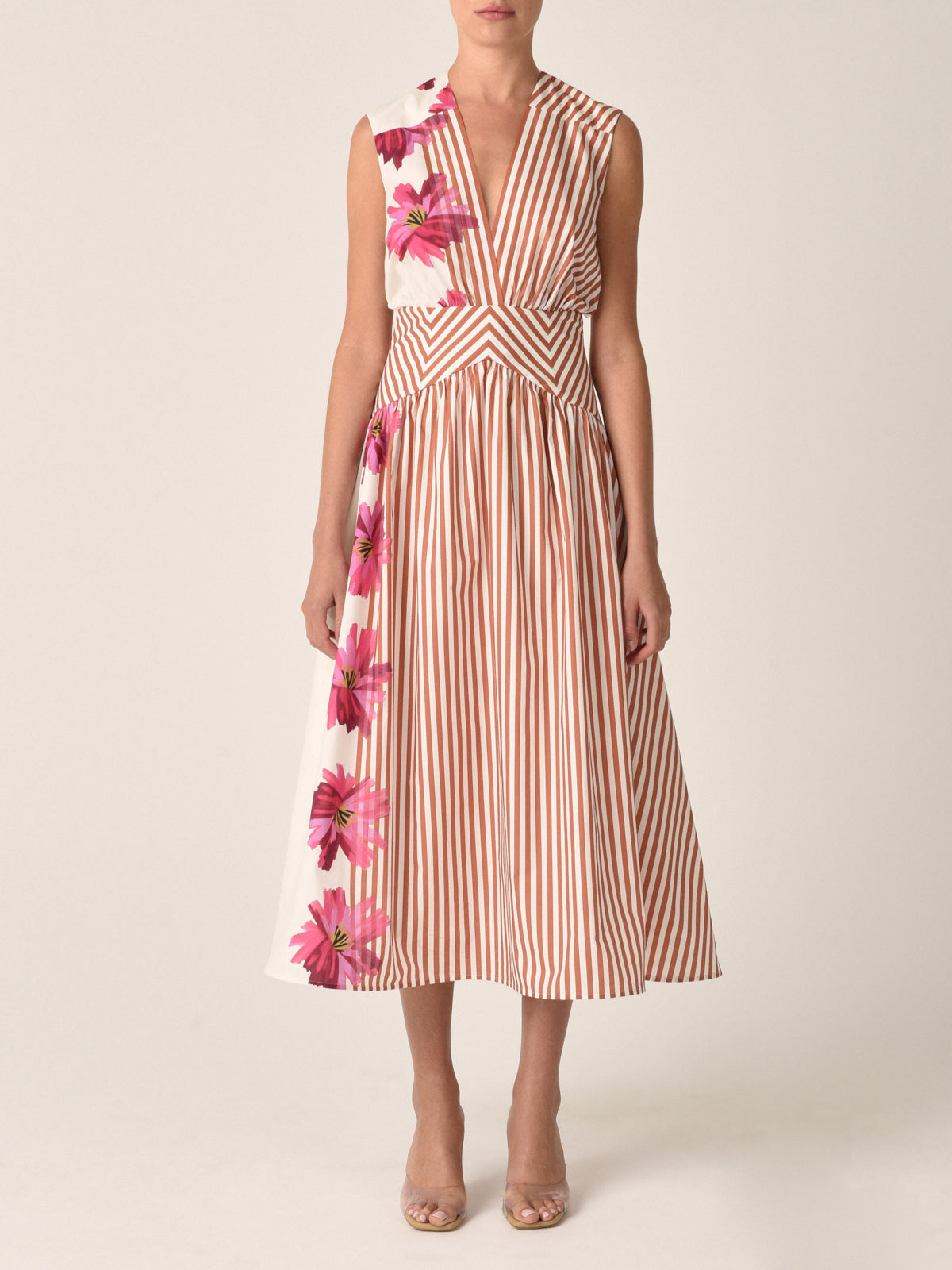 A woman is stylishly dressed in the Jocelyn Dress in Magenta Floral Brushstroke Stripes, featuring vertical orange accents, and paired with open-toed shoes for a charming daytime ensemble.