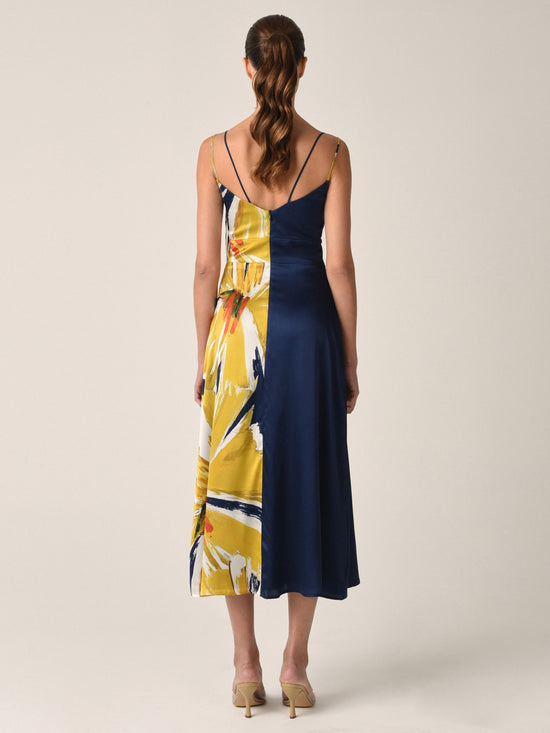 The Lizzo Dress Navy Floral Brushstrokes is a silk navy midi dress with spaghetti straps, showcasing a large yellow and white floral print alongside an A-line skirt.