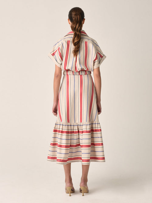 A person wearing the Loni Dress in natural teal coral stripes stands facing backward, showcasing its cinched waist and ruffled hem.