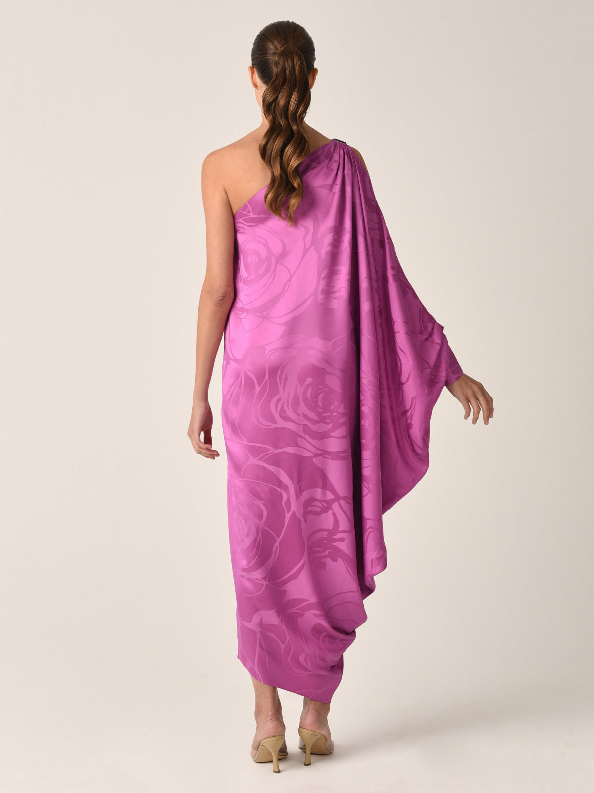 The Marcelin Dress in Magenta Orchid Jacquard features a one-shoulder design with a floral pattern and a flowing asymmetrical hemline.