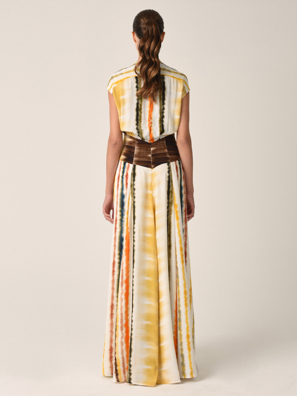 The Marion Dress Multi Hazy Stripe from the Resort 2023 collection features a sleeveless, floor-length design with a multi hazy stripe print in yellow, orange, and brown. It boasts a v-neckline and keyhole opening at the back.