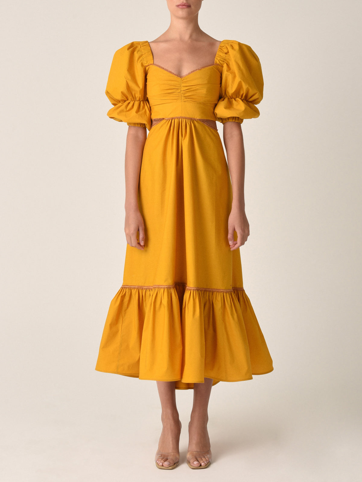 Introducing the Peggie Dress Marigold, a stunning Silvia Tcherassi dress in mustard yellow, featuring puffed sleeves, a fitted bodice, side cutouts, and a ruffled hem—an essential piece from Resort 2023.