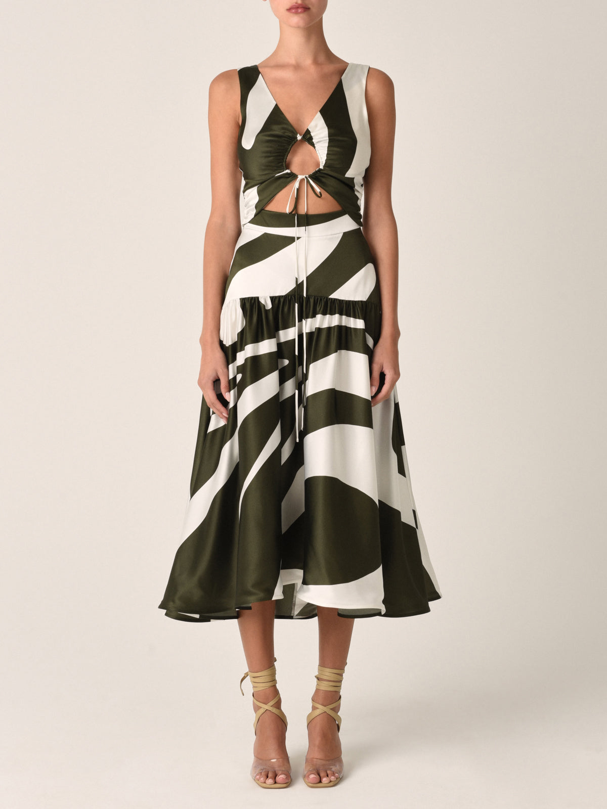 Experience elegance in the Roseanne Dress Green Abstract Palm, a sleeveless silk midi dress with a striking black and white abstract pattern. The gathered front bodice and asymmetrical hemline add an extra touch of sophistication to this timeless piece.