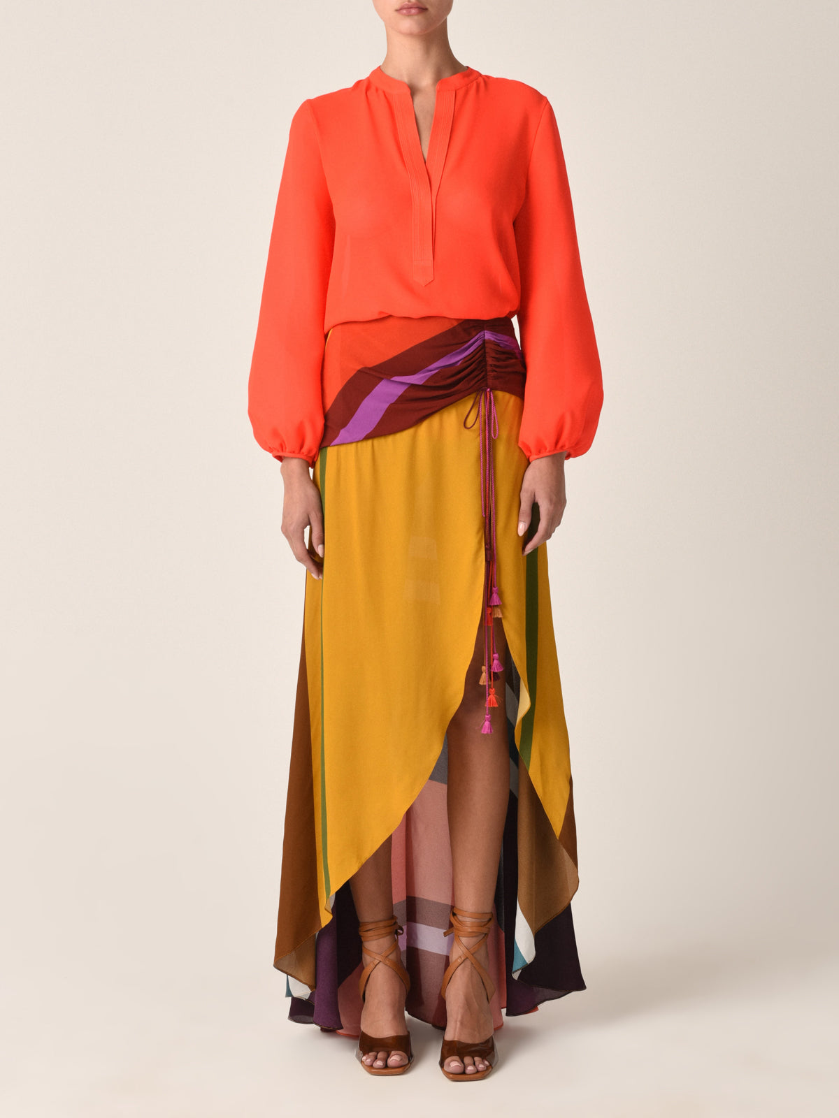 The Triora Blouse Tangerine is a lively tangerine-colored viscose top with a V-neckline, complemented by flowing long sleeves and relaxed cuffs, shown against a plain white background.