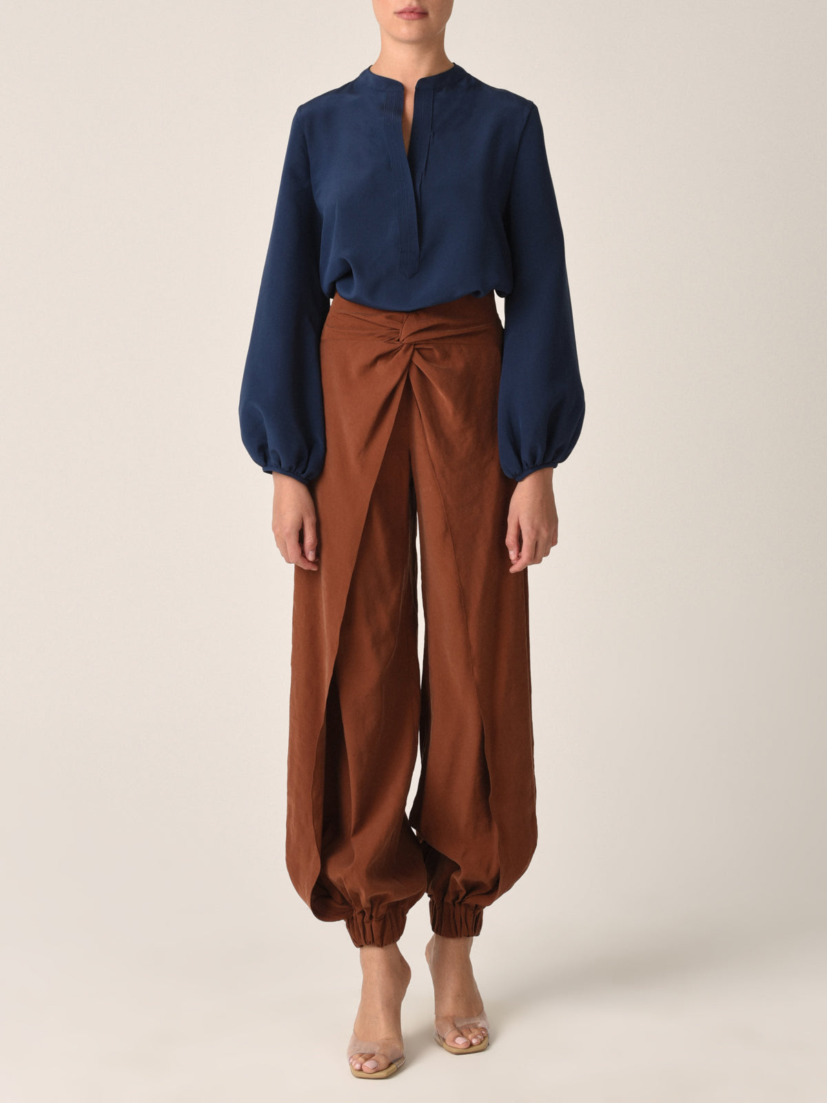 The Raimondo Pant Cacao, featuring a high-waisted design with a twisted front detail and gathered cuffs, pairs perfectly with our honey blouse crafted from luxurious vegan silk.