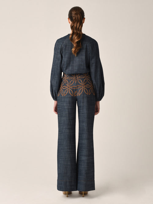 A dark blue long-sleeved Vigolene Blouse Chambray Embroidery featuring an intricate geometric pattern in orange. The high-fashion sleeves add an elegant touch, while a tie at the neckline with tassels completes this chic look.