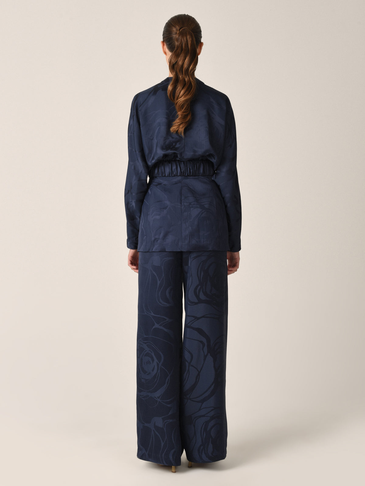 Casey Pant Navy Jacquard, these high-waisted, wide-leg pants featuring a subtle floral pattern in luxurious jacquard fabric and a gathered waistband detail.