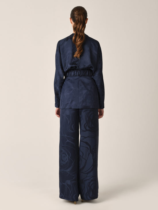 Casey Pant Navy Jacquard, these high-waisted, wide-leg pants featuring a subtle floral pattern in luxurious jacquard fabric and a gathered waistband detail.