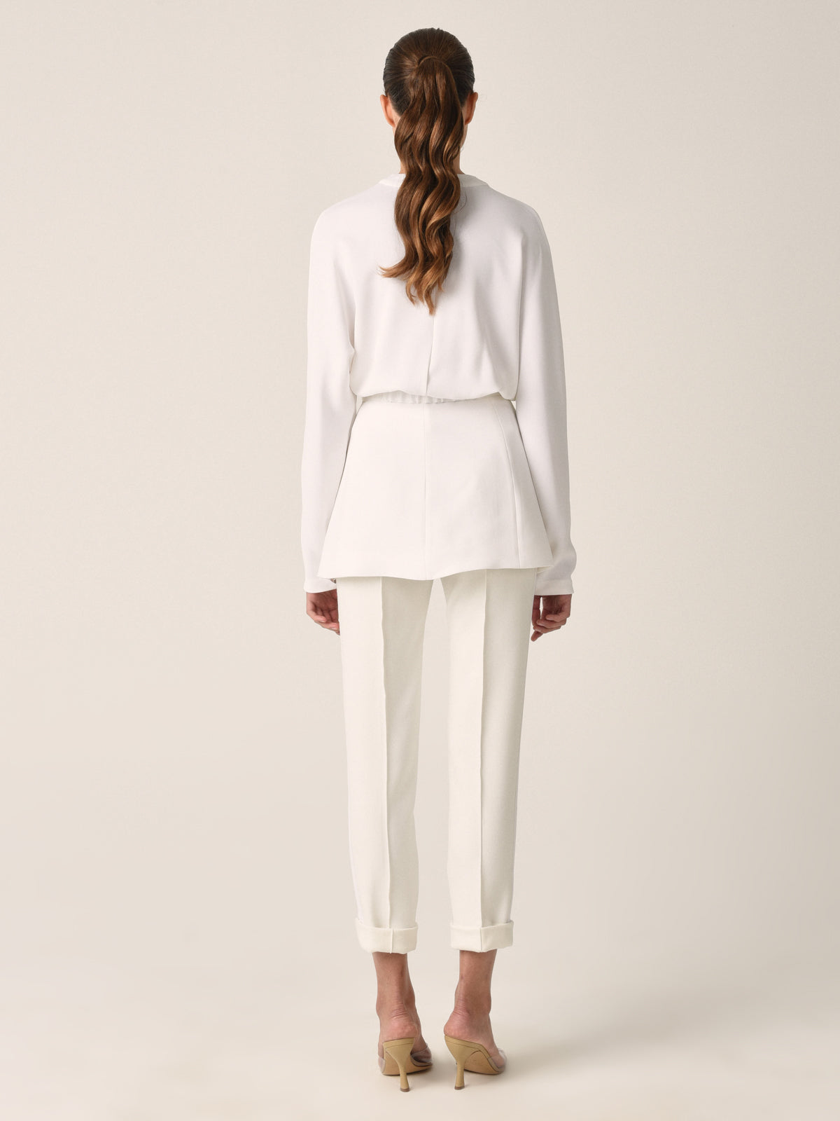 A white belted blazer with long sleeves, two front pockets, and a V-neck collar photographed against a plain background exudes modern elegance. This seasonless sleek white viscose piece, known as the Vogogna Jacket White, is a timeless addition to any wardrobe.